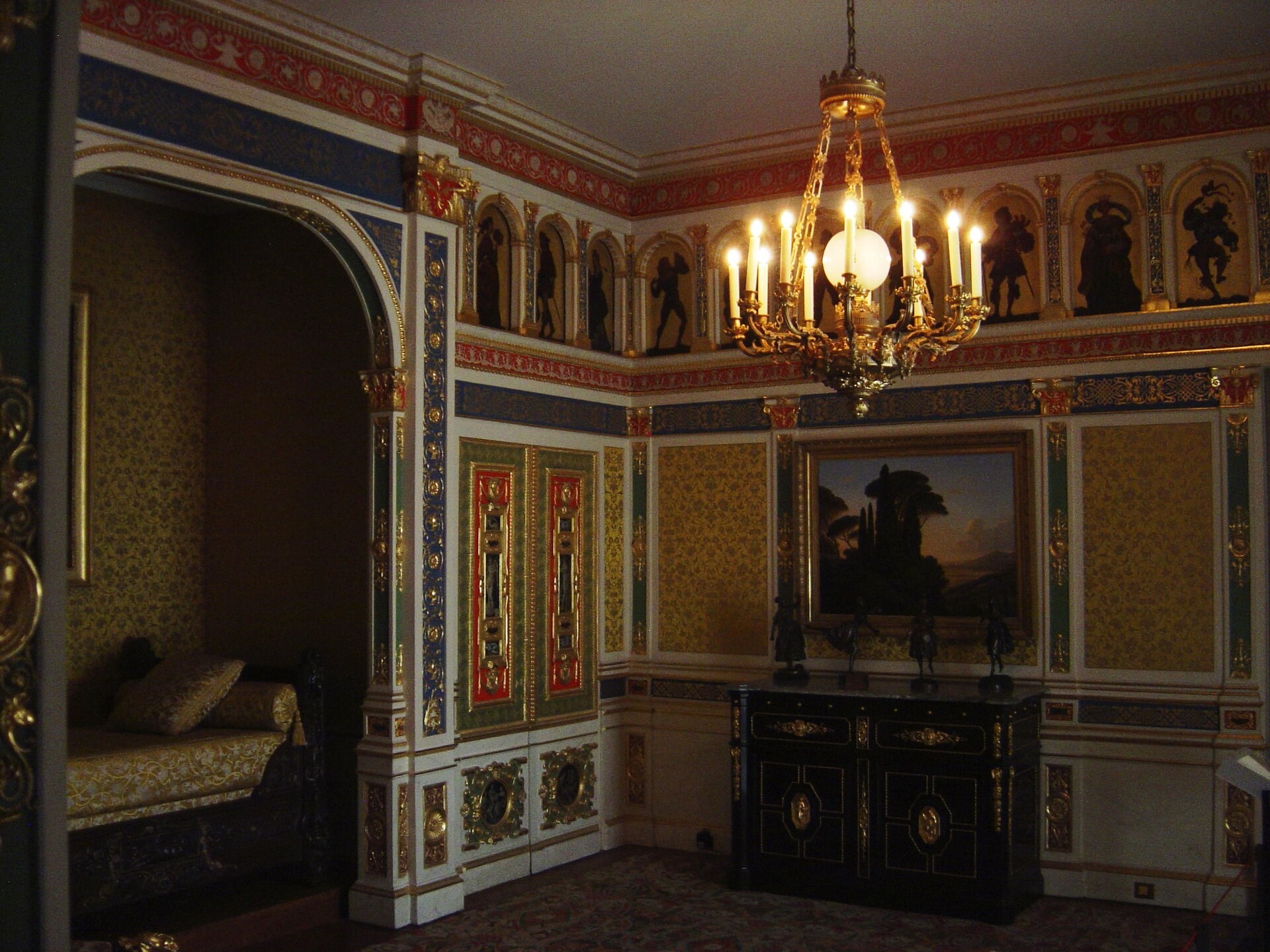 A chandelier and framed pictures hang above red-and-gold panels in the reconstructed Hope bedroom at MAD.