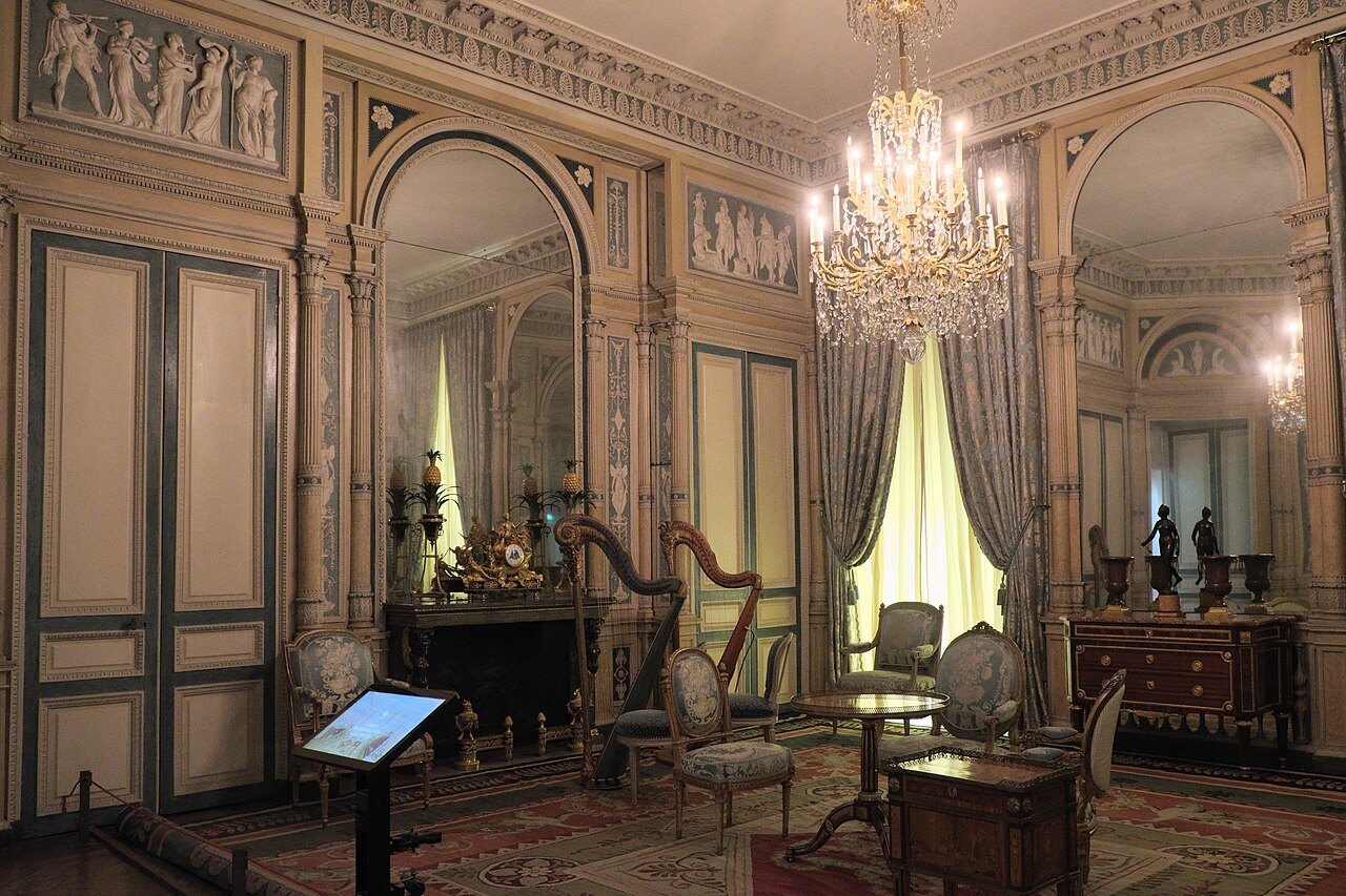 An elegant historic salon with mirrored wall panels, a chandelier, harp and gilded chairs.