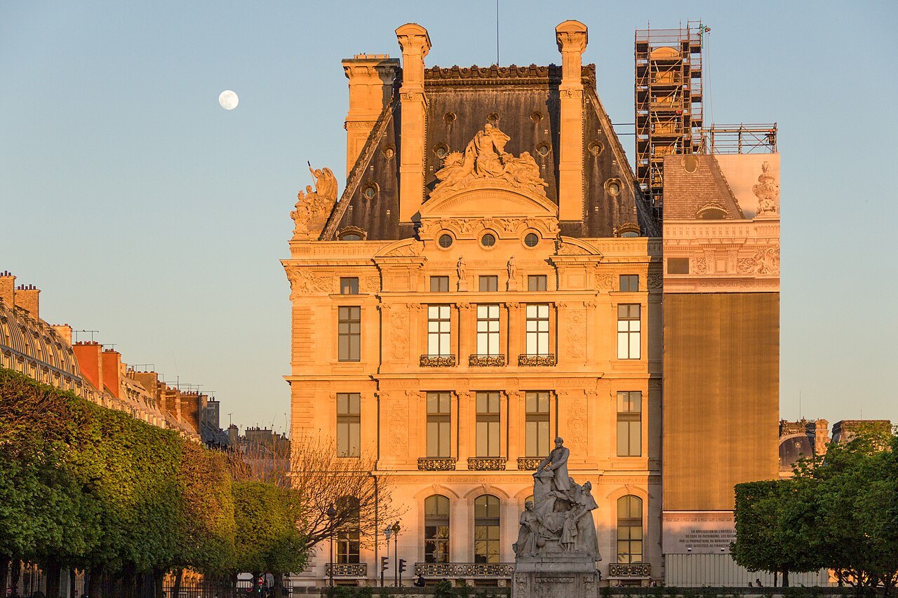 The historic Pavillon de Marsan façade glowing gold beside the Tuileries, with the moon overhead.
