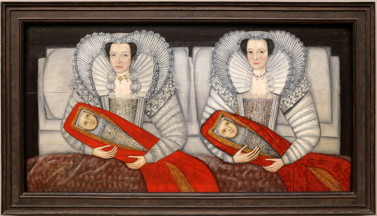 Two women sit side by side, each holding a swaddled baby.
