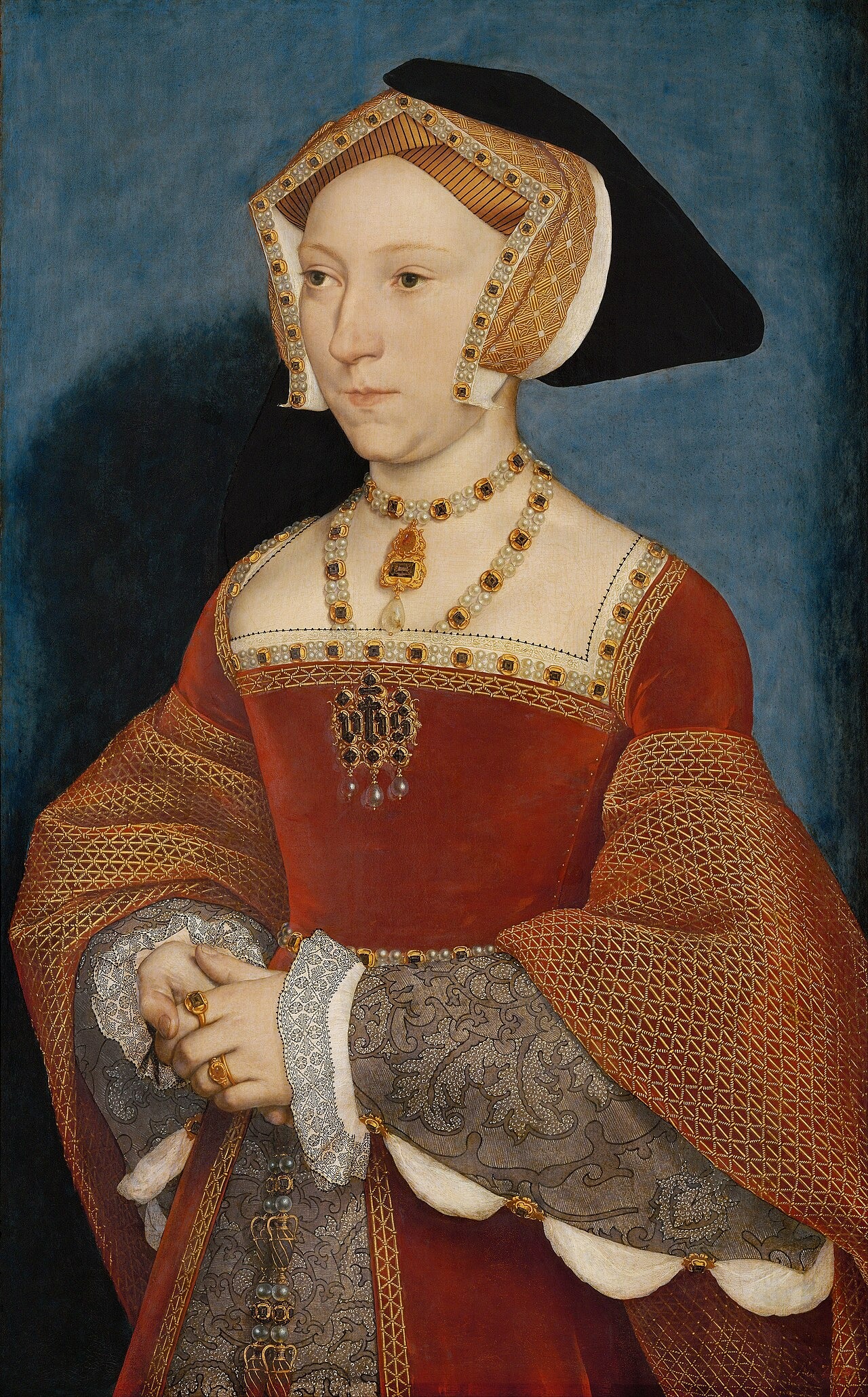 A woman in a red gown, embroidered sleeves and a peaked headdress stands against a blue background.