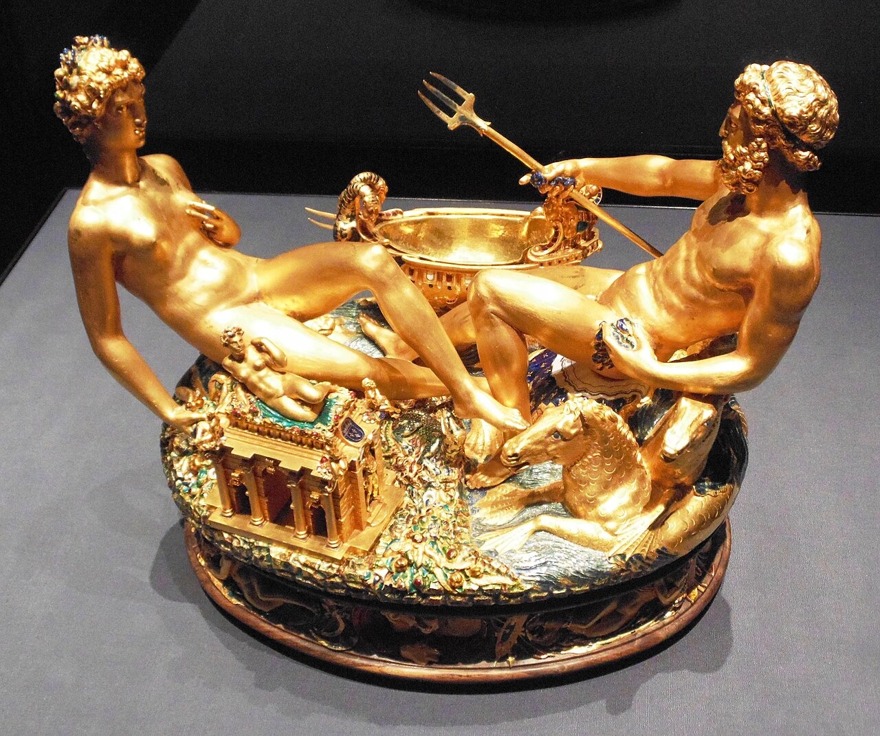 Two reclining gold figures face each other across a small ship on an oval ornamental base.
