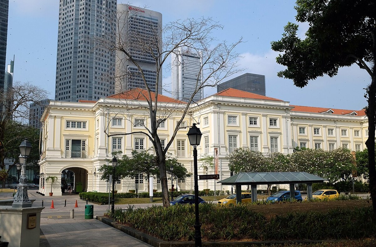 Cream-coloured Asian Civilisations Museum building with a terracotta roof, trees and a city skyline behind it.