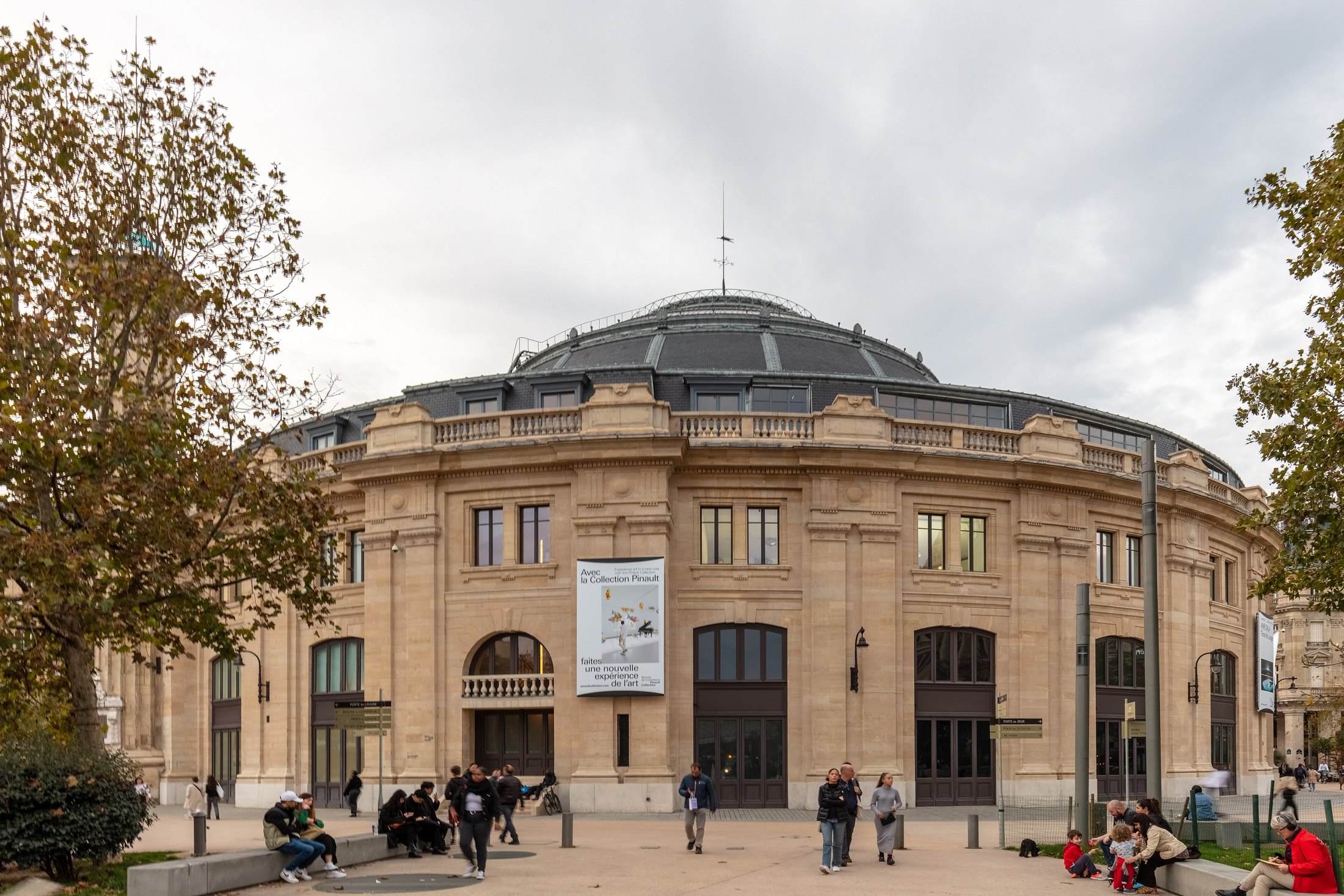 The Bourse de Commerce’s circular stone façade framed by autumn trees, with visitors outside