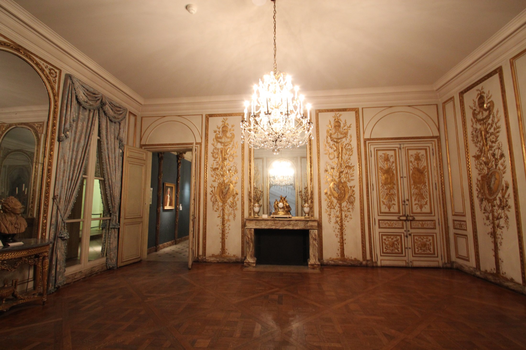 A chandelier, gilded wall panels and a marble fireplace in a historic salon at Musée Carnavalet