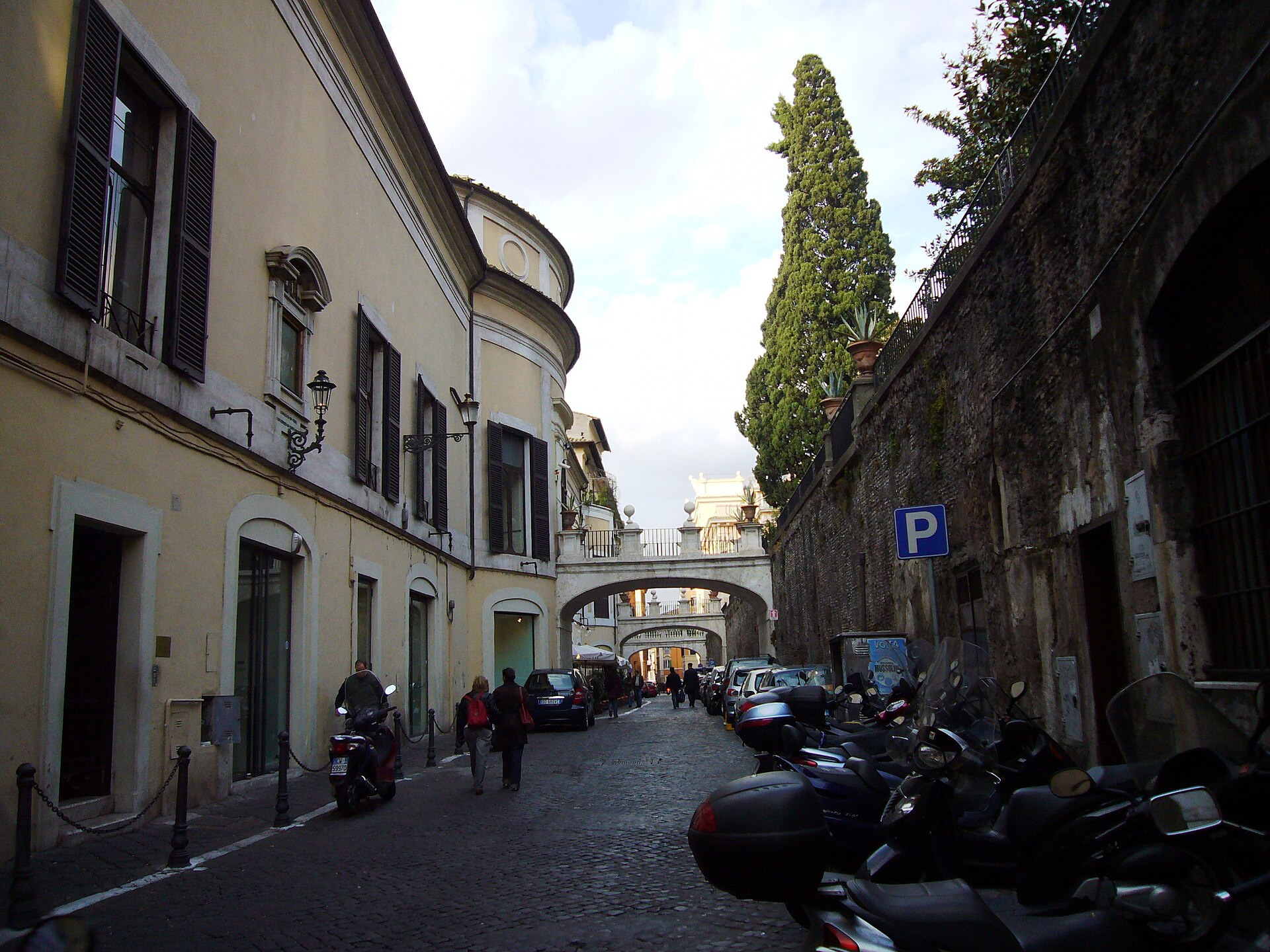 Cobblestoned Via della Pilotta, scooters and stone arches beside Palazzo Colonna