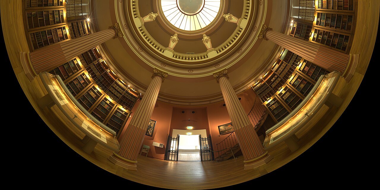 A wide-angle view of the circular historic library, with stacked bookshelves, columns and a skylight.