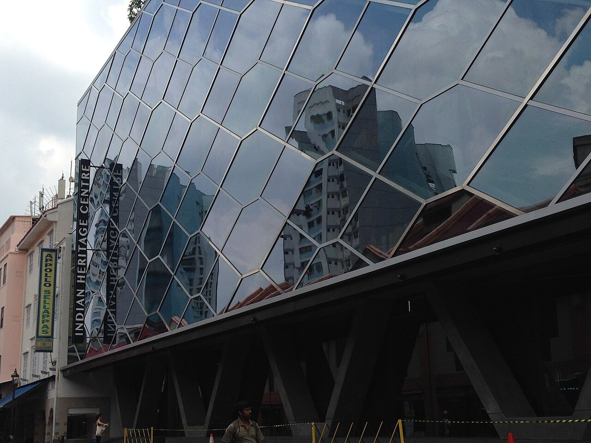 Faceted glass facade of the Indian Heritage Centre reflecting neighbouring Little India buildings.