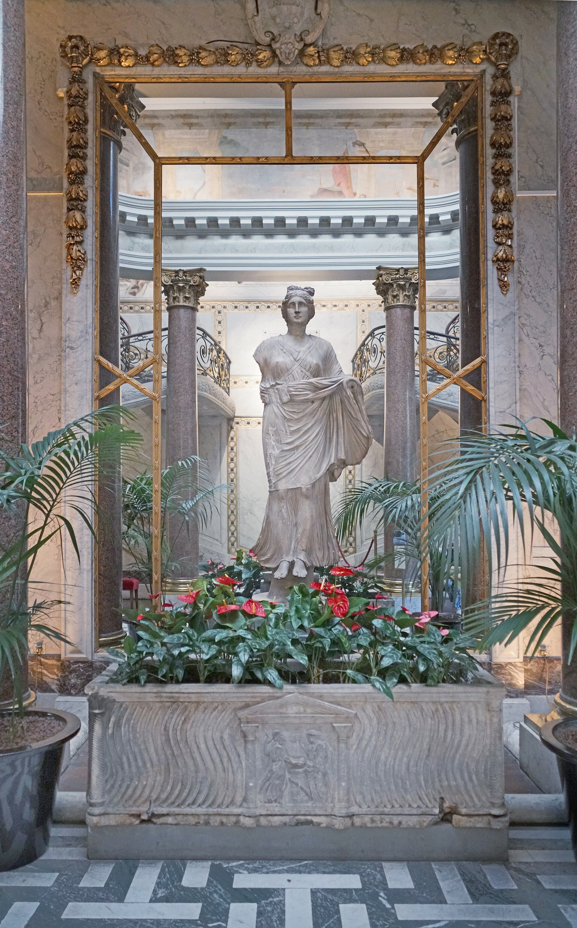 An ancient marble statue and carved Roman sarcophagus among plants in Musée Jacquemart-André’s winter garden