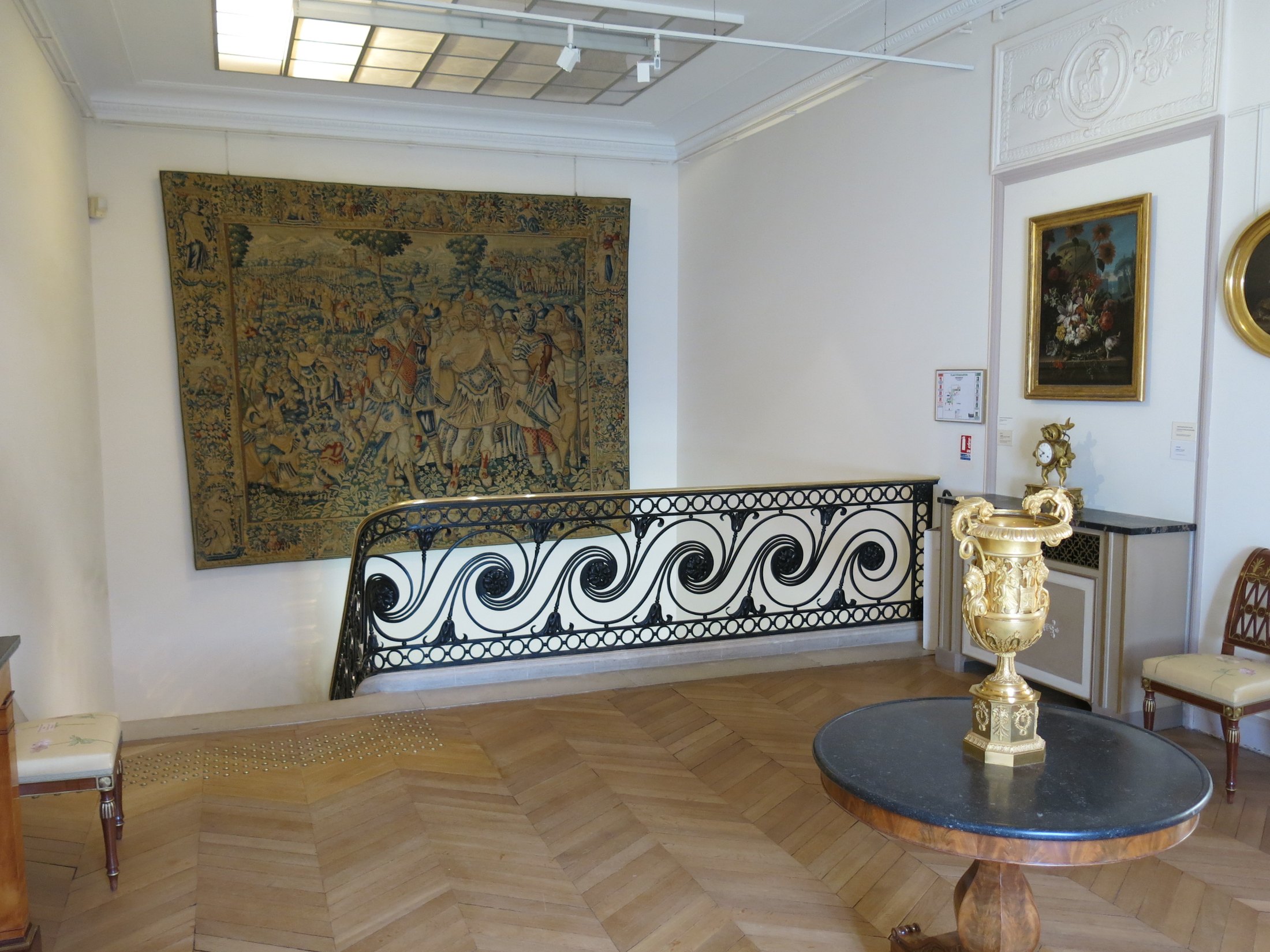 A decorative iron stair rail, an old tapestry and a gilded urn inside Musée Marmottan Monet