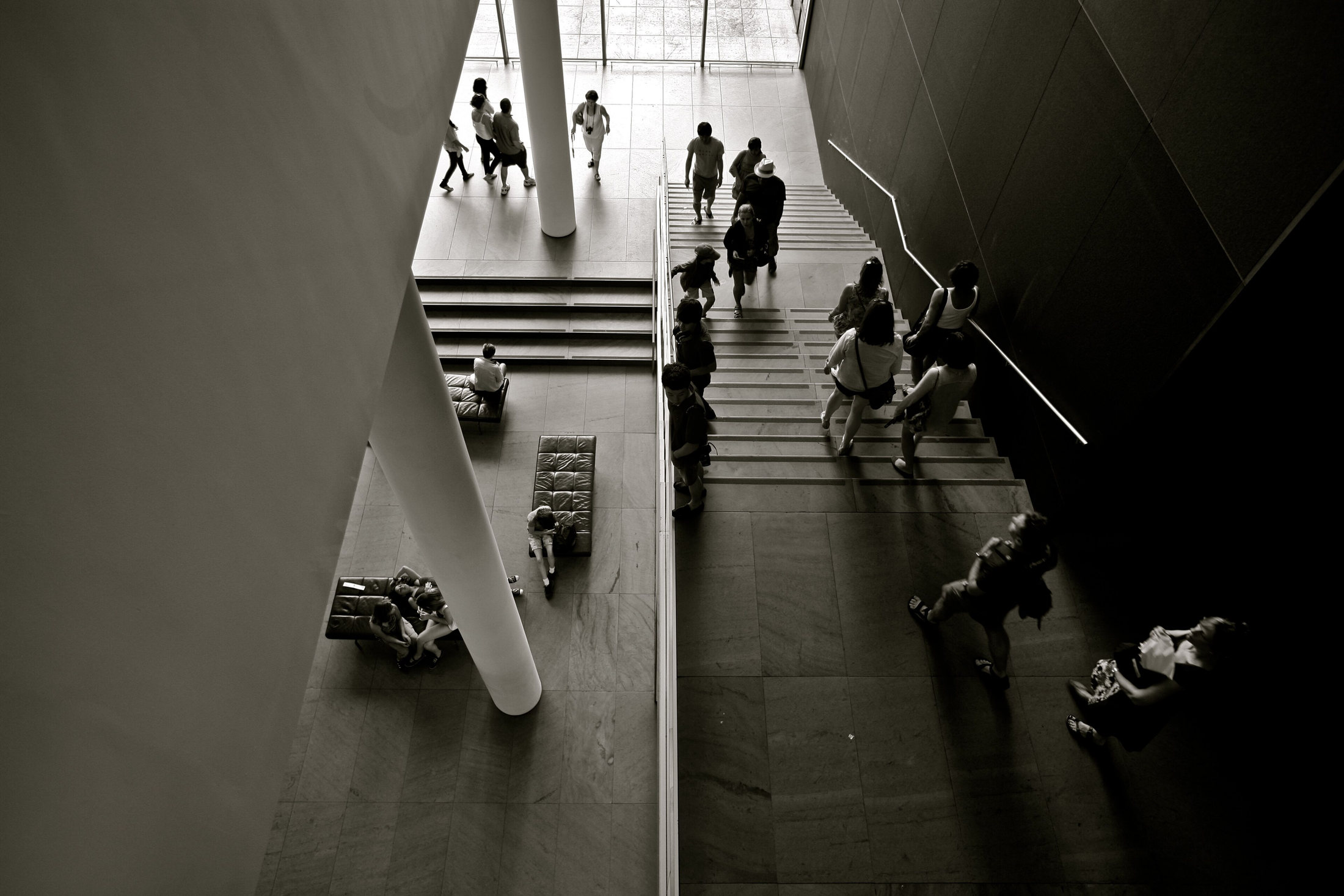 Visitors moving through MoMA’s angular indoor staircase, in black and white