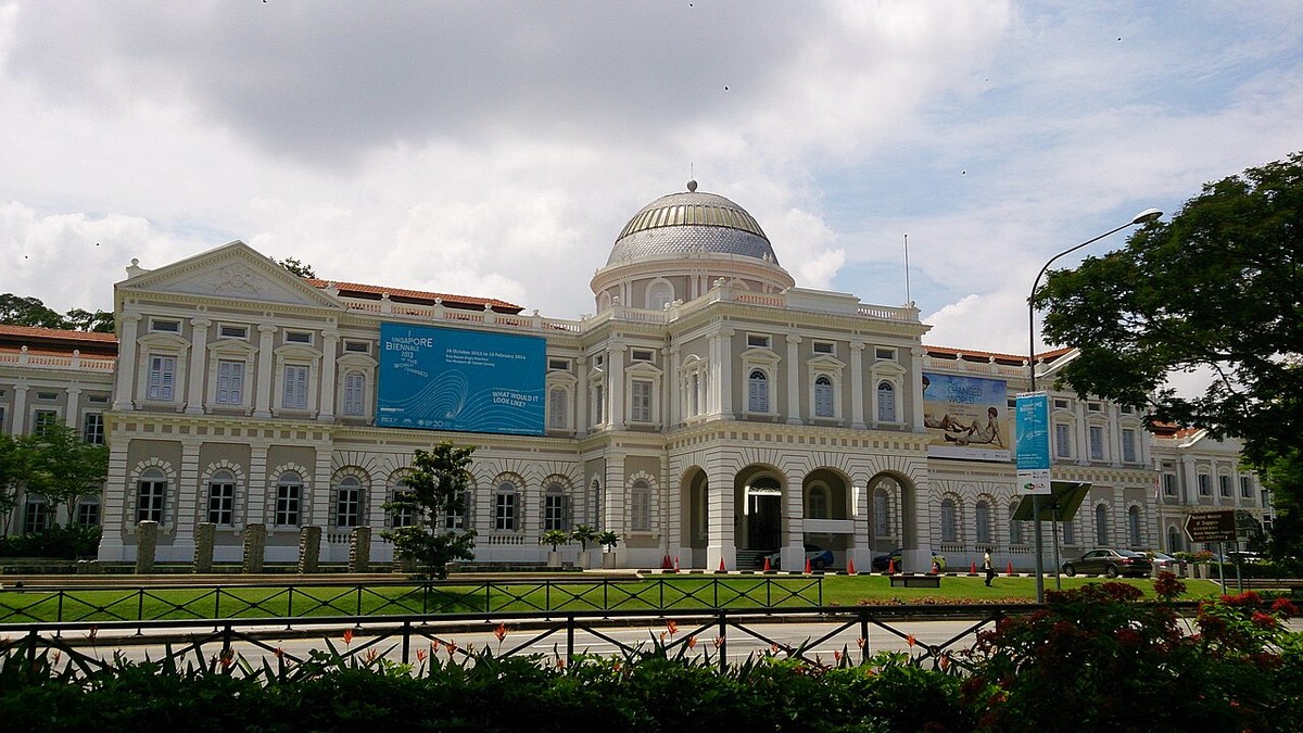 Pale neoclassical facade and central dome of the National Museum of Singapore behind a green lawn.