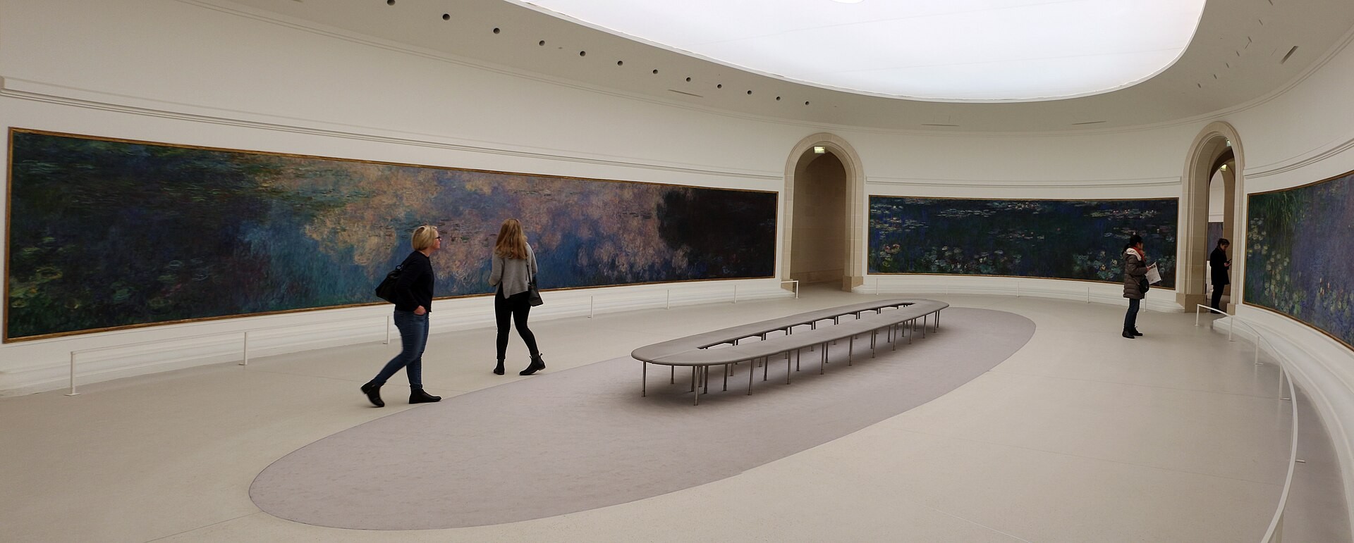 Visitors and an oval bench sit within the curved Water Lilies gallery at Musée de l’Orangerie.