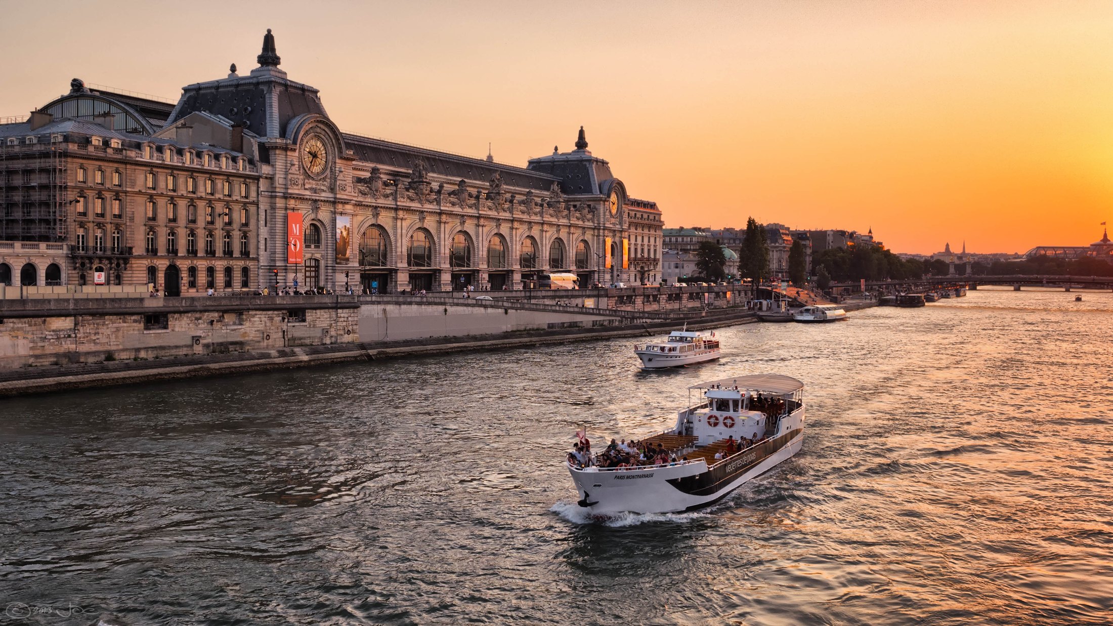 Musée d’Orsay beside the Seine under an orange sunset, with river boats in the foreground