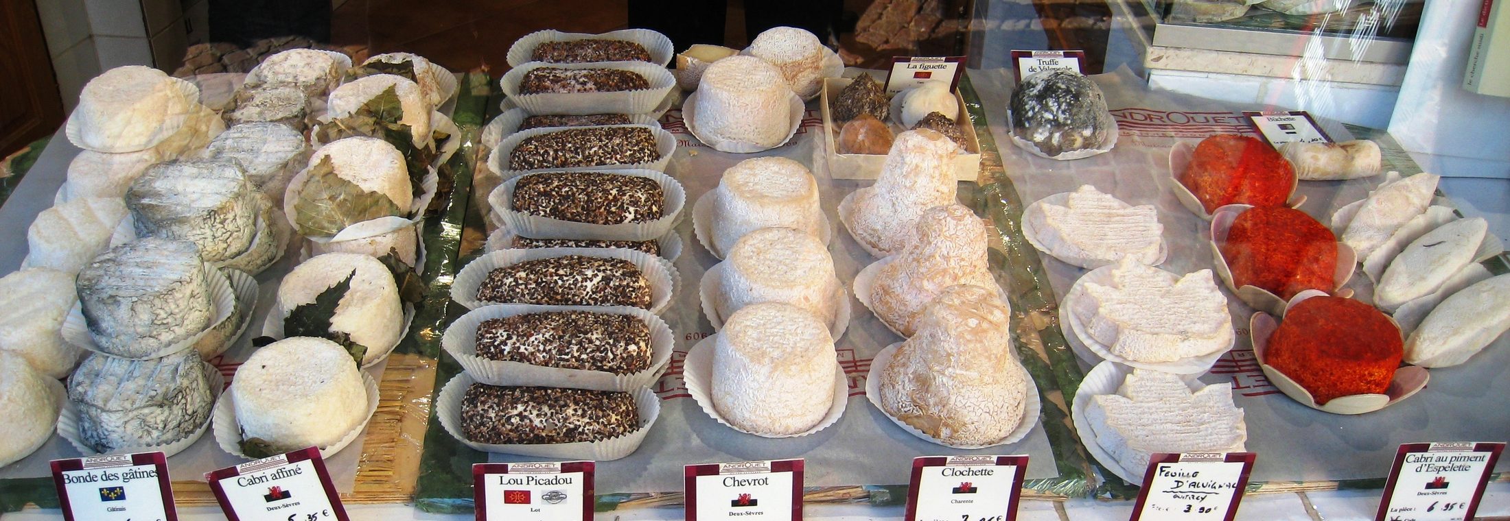 Assorted cheeses arranged in rows behind a Paris market counter