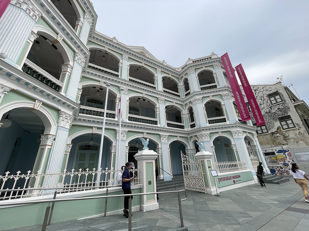 Pale green and white Peranakan Museum facade with arched verandas and the entrance gate.