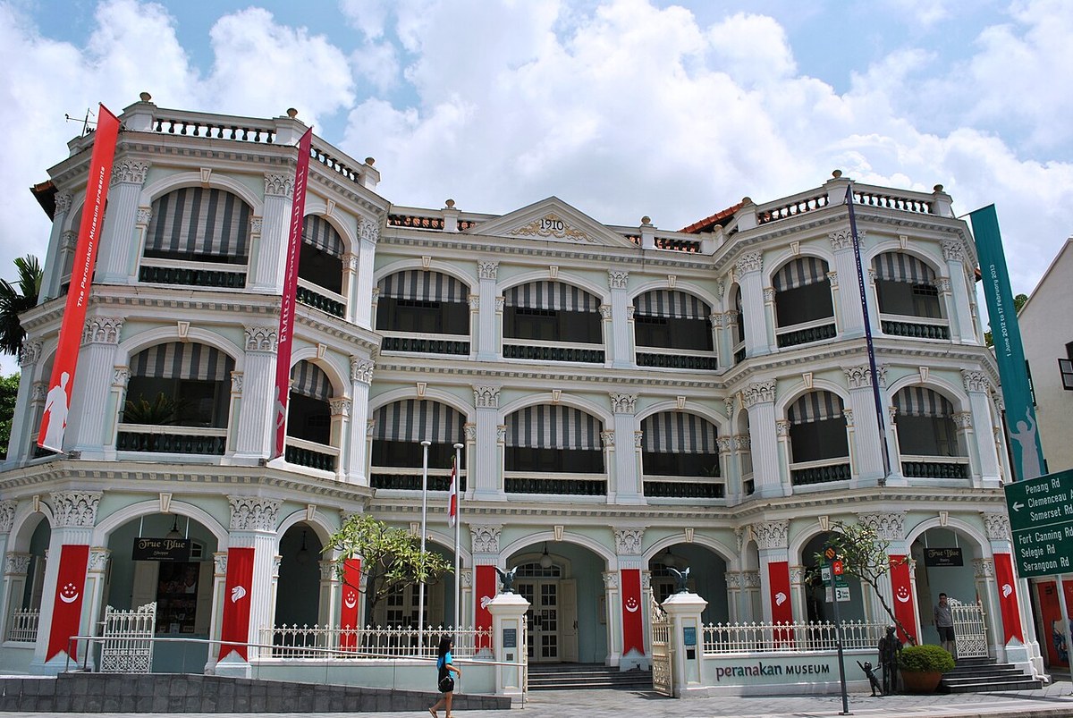 Front view of the Peranakan Museum with ornate white balconies, arched windows and red vertical banners.