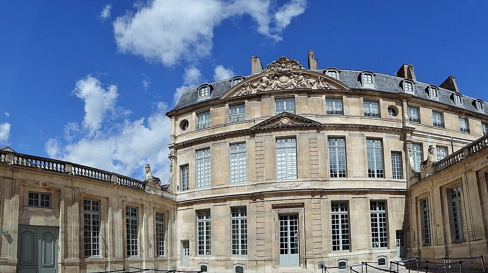 An angled view of Hôtel Salé’s stone courtyard façade under a blue sky