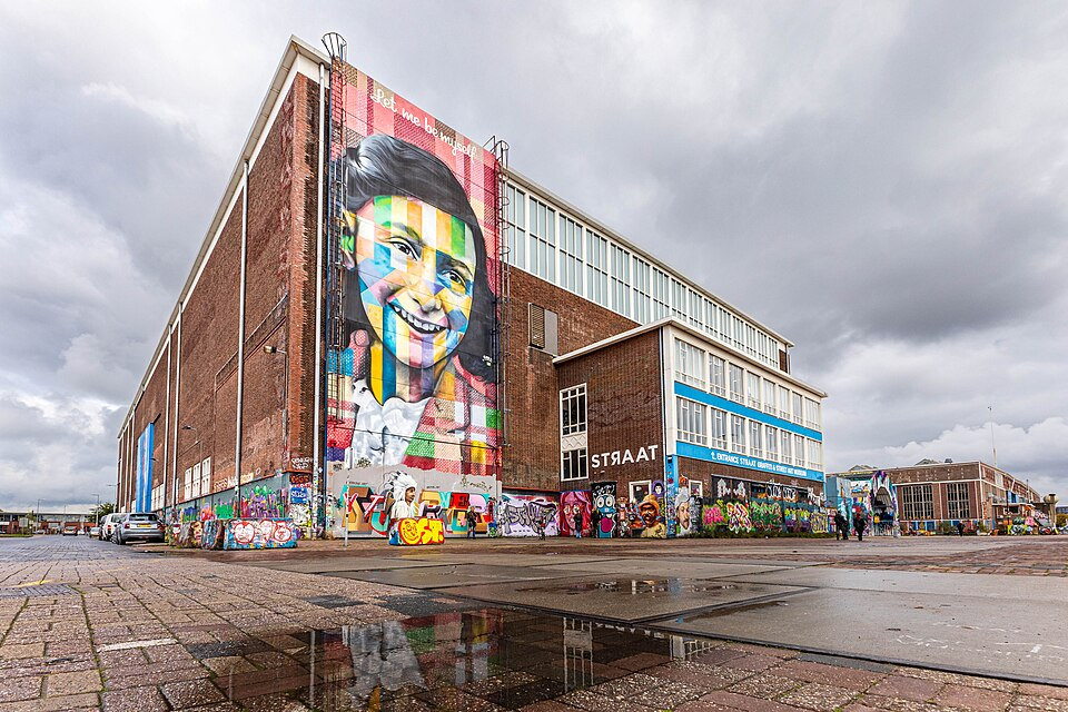 STRAAT Museum’s brick warehouse reflected in a puddle beside the Anne Frank mural
